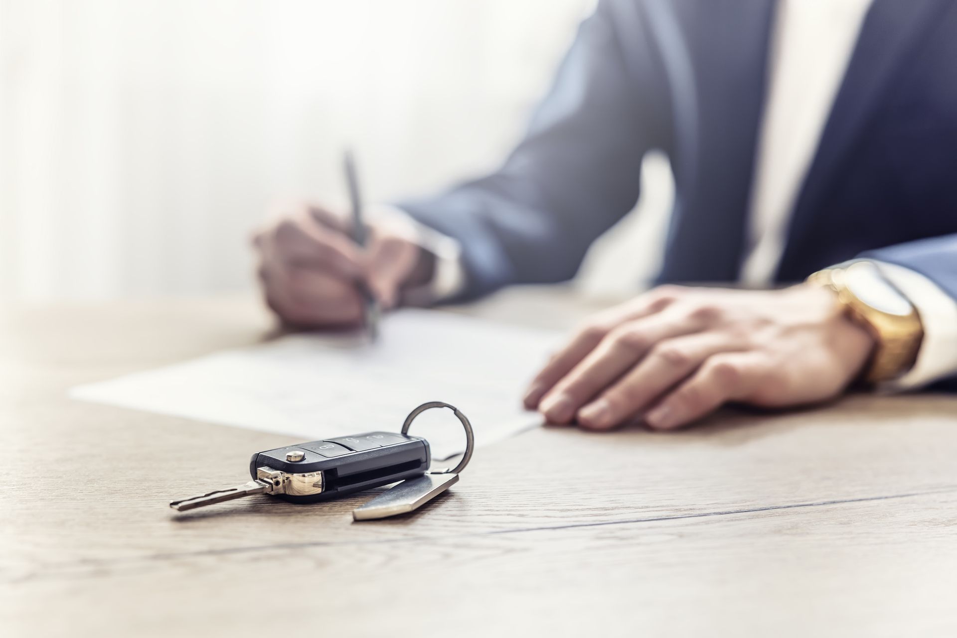 Male client in a suit signing an auto insurance contract. New car keys in the foreground.