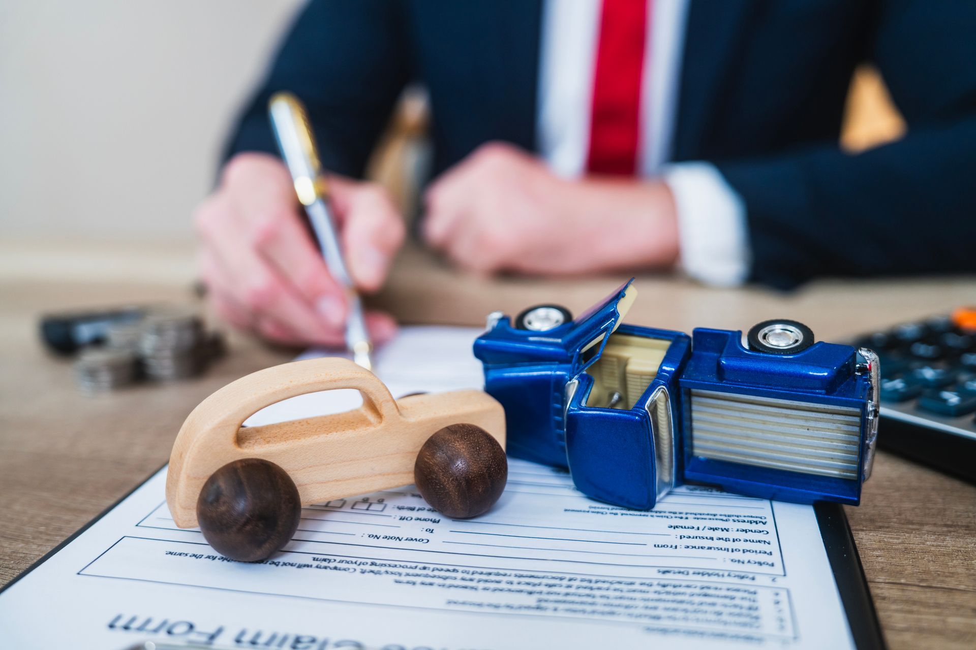 Closeup of toy cars on auto insurance claim form in office setting with businessperson.