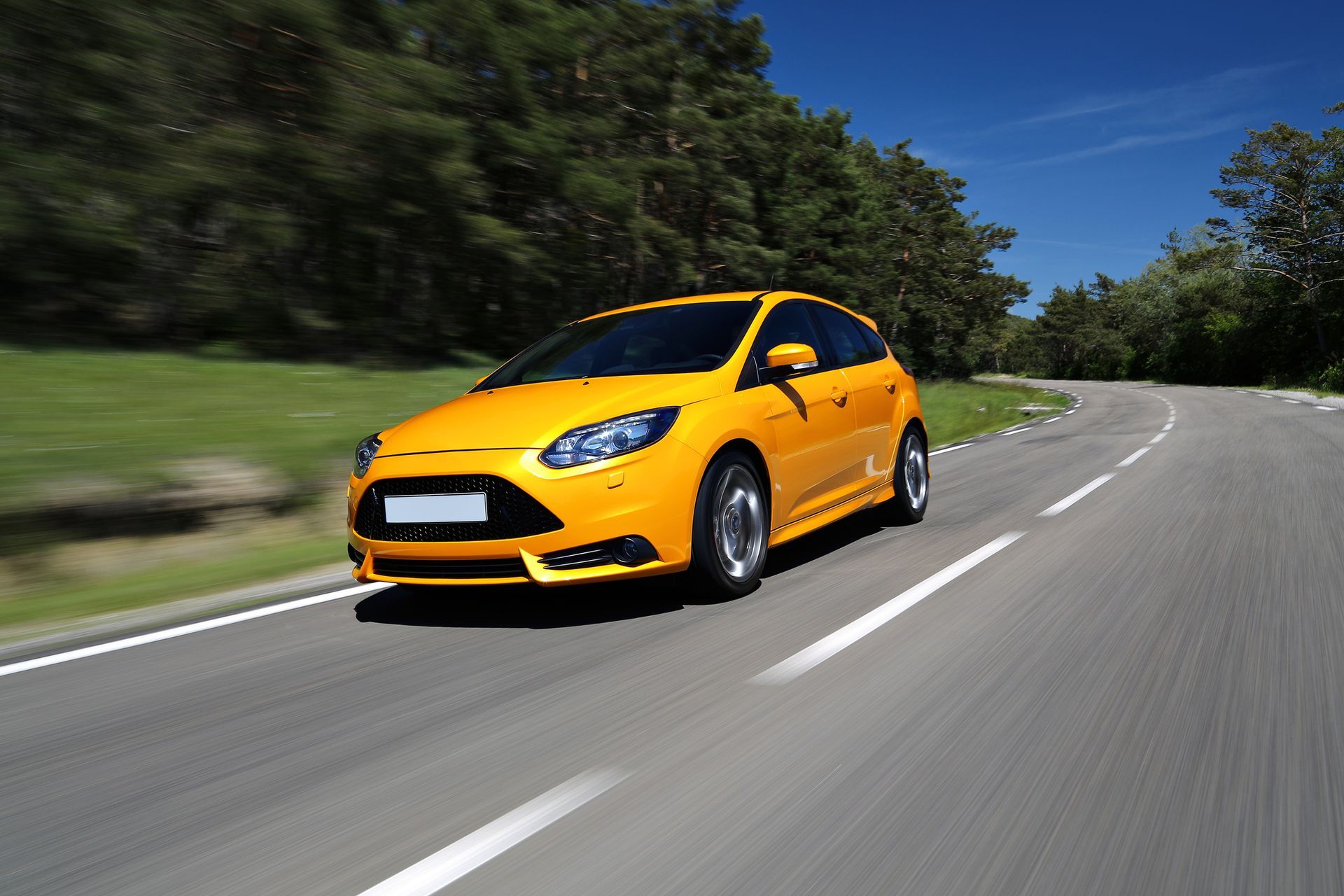 A wide view of a yellow sports car drives along a winding forested road.