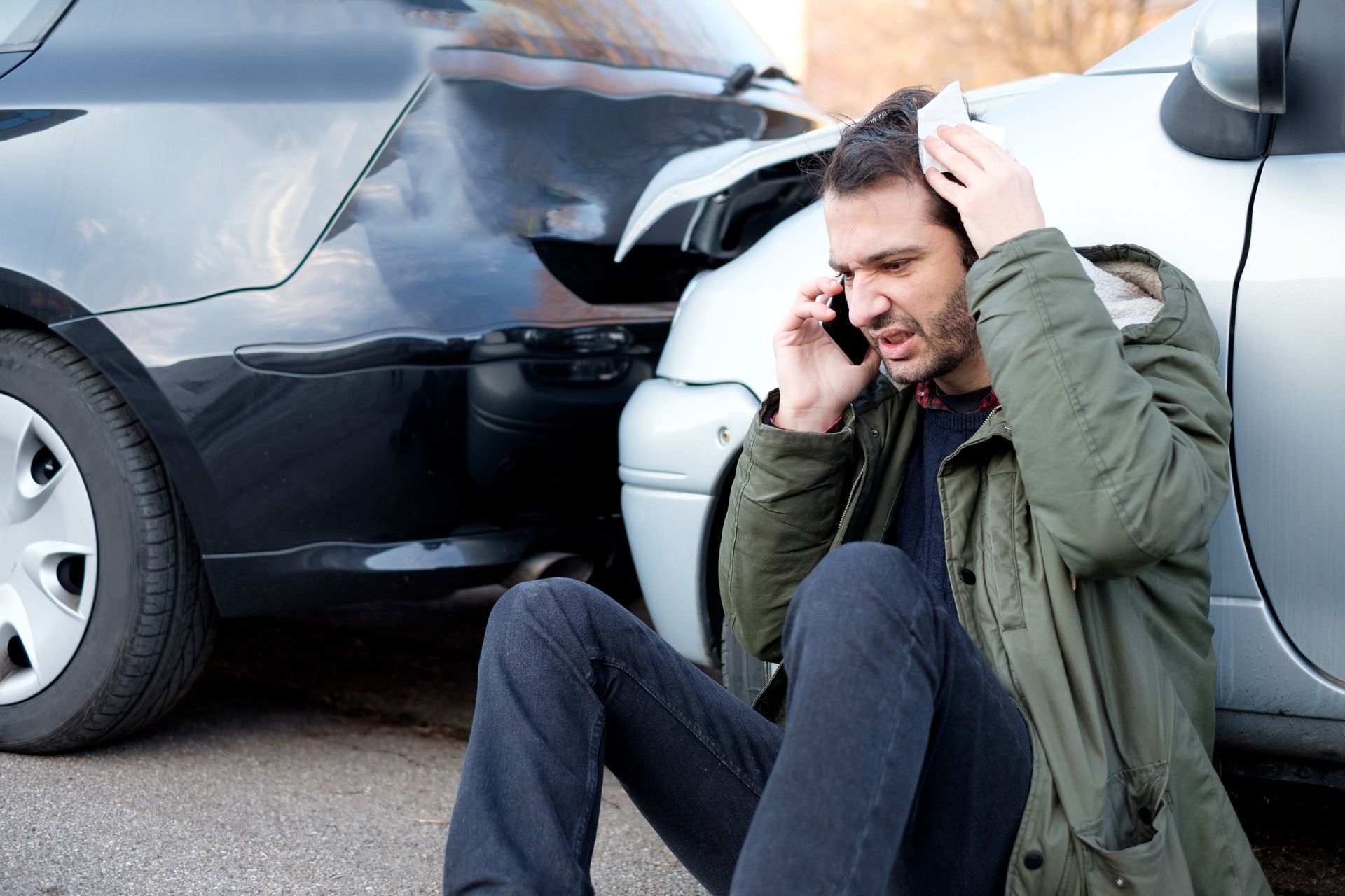 A person talking on the phone to his Auto Insurance Coverage next to a broken car