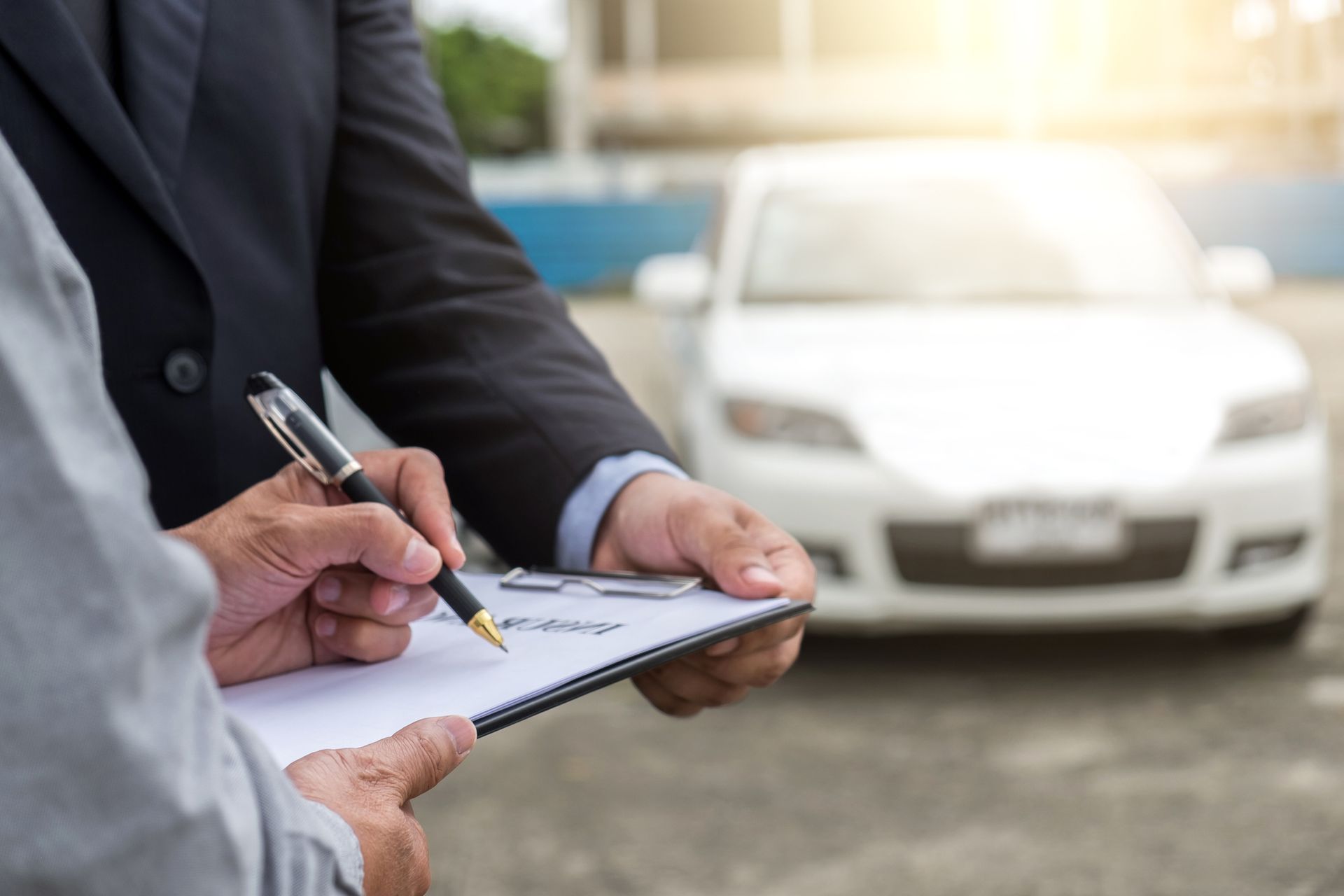 Signing car insurance documents outdoors with vehicle in background.