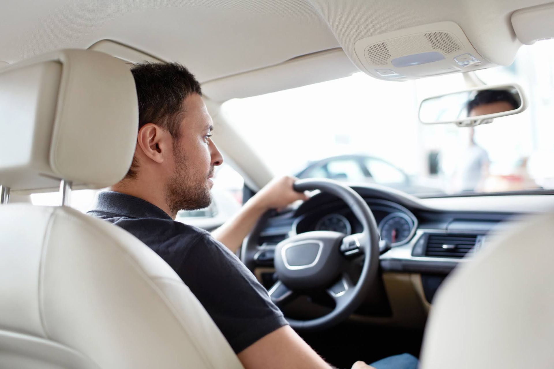Man driving a modern car, viewed from the back seat.
