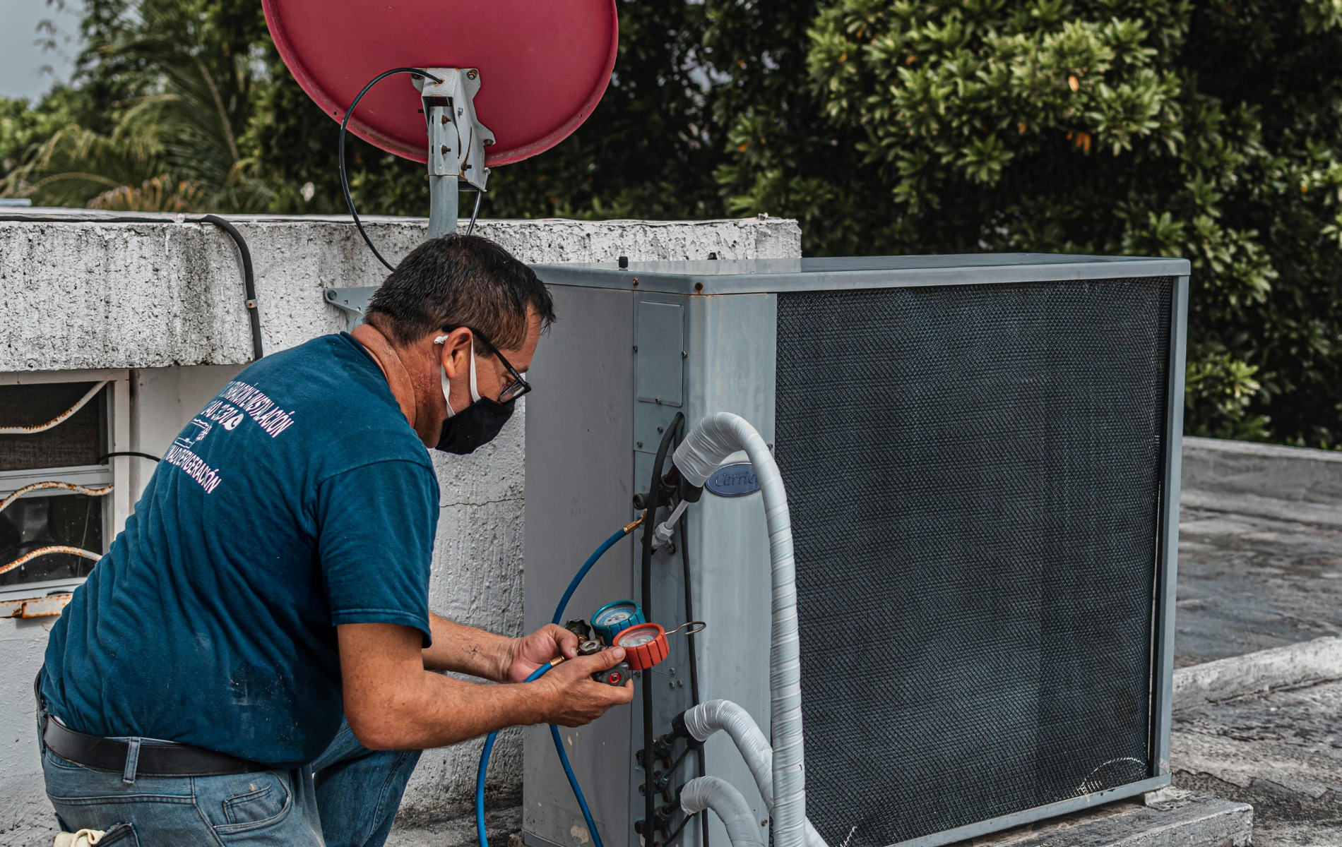 A man wearing a mask is working on an air conditioner on a roof.