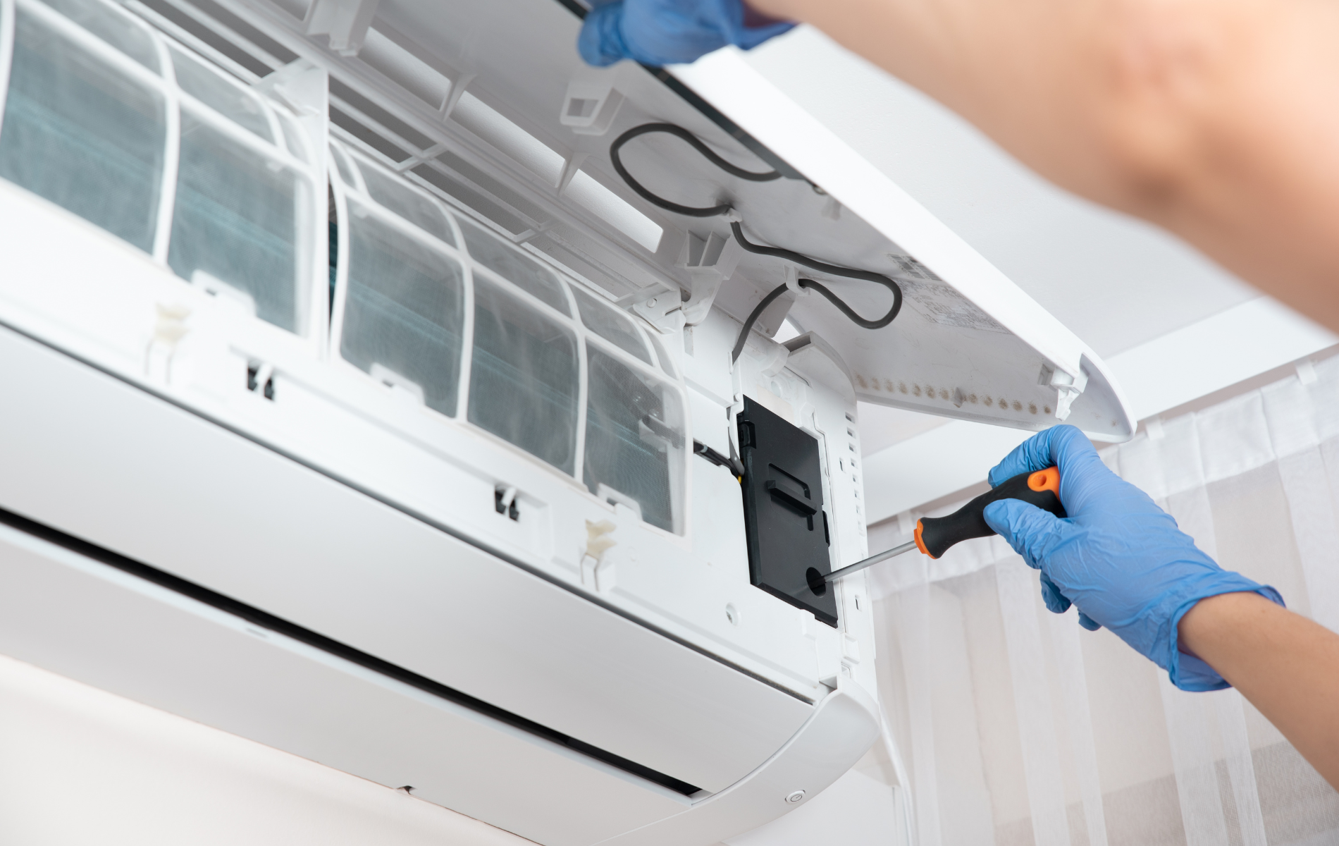 A person is fixing an air conditioner with a screwdriver.