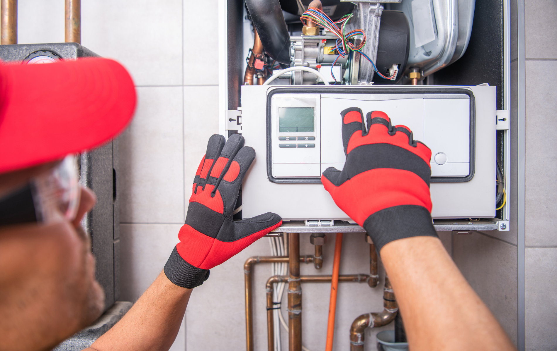 A man wearing red and black gloves is working on a boiler.