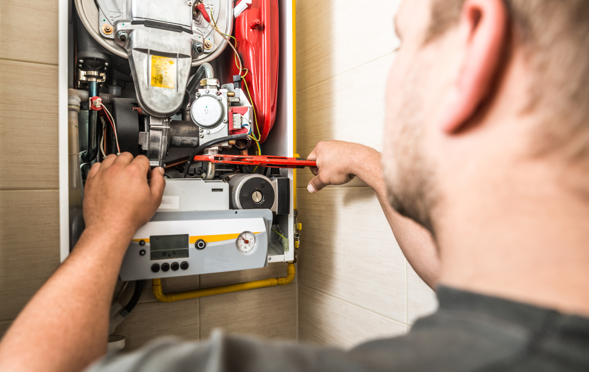 A man is fixing a boiler with a wrench.