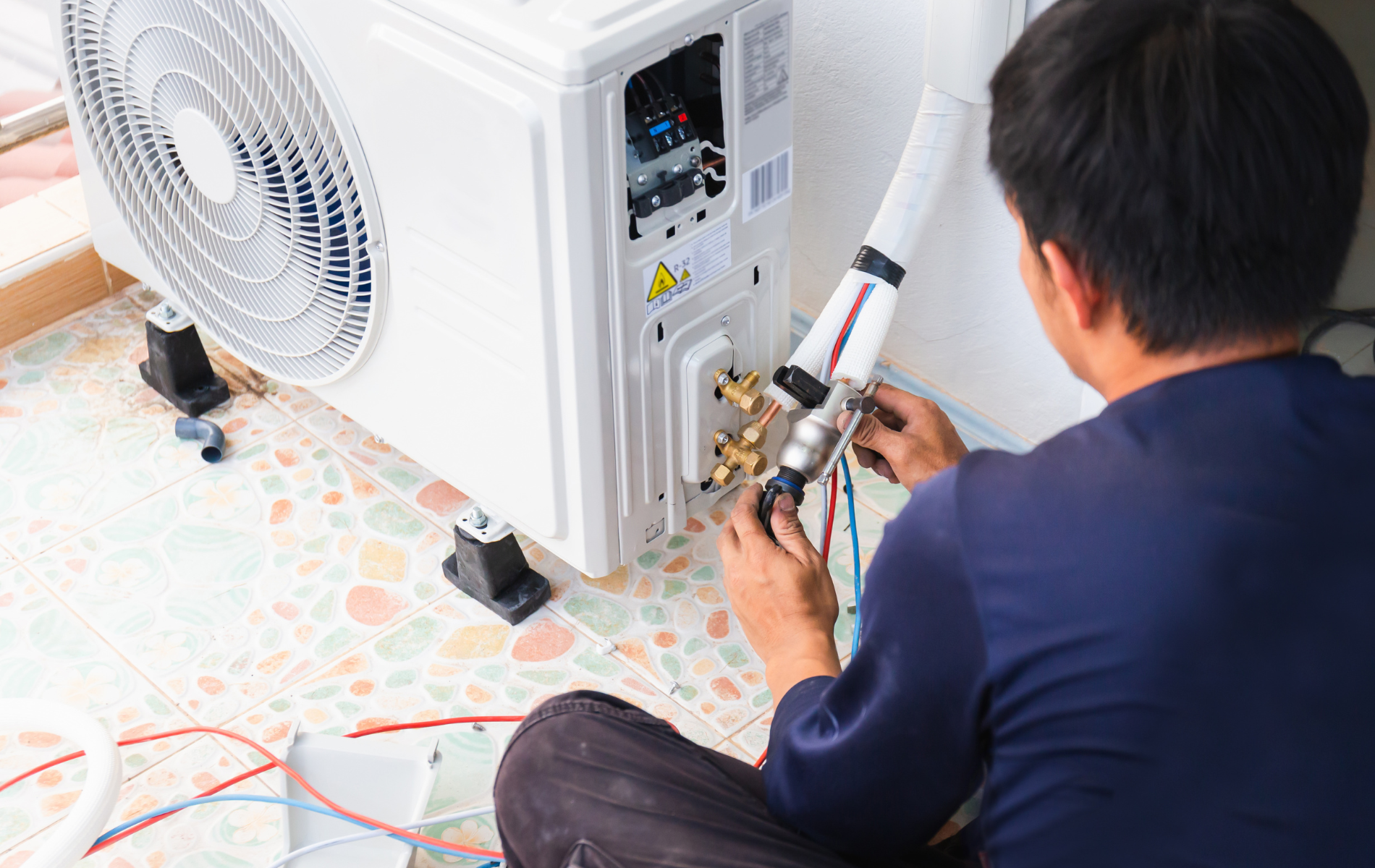 A man is sitting on the floor fixing an air conditioner.