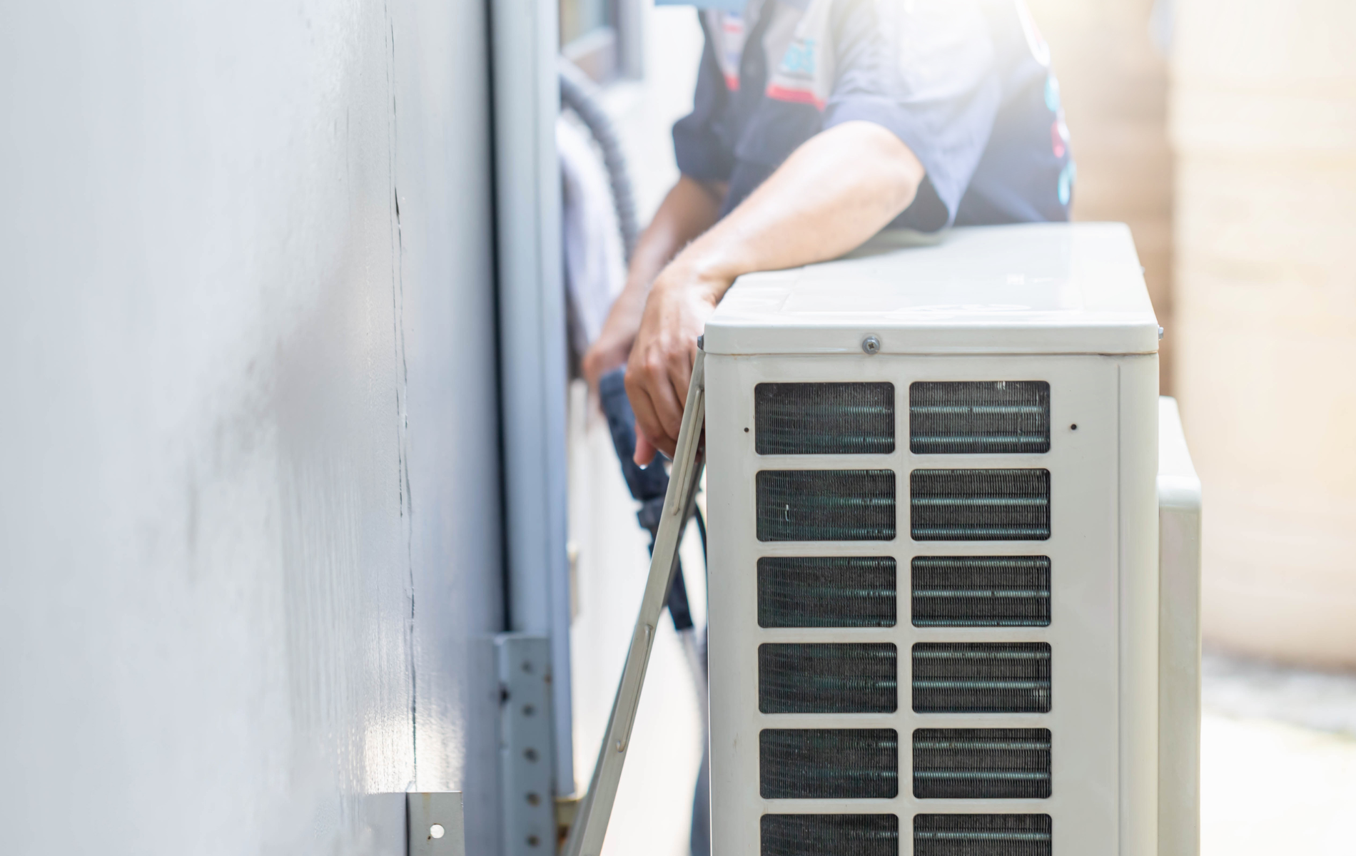 A man is installing an air conditioner on the side of a building.