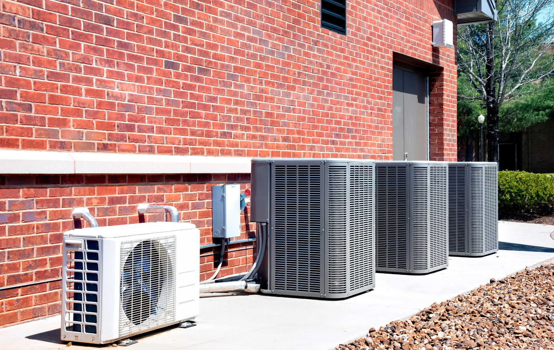 A row of air conditioners are sitting outside of a brick building.