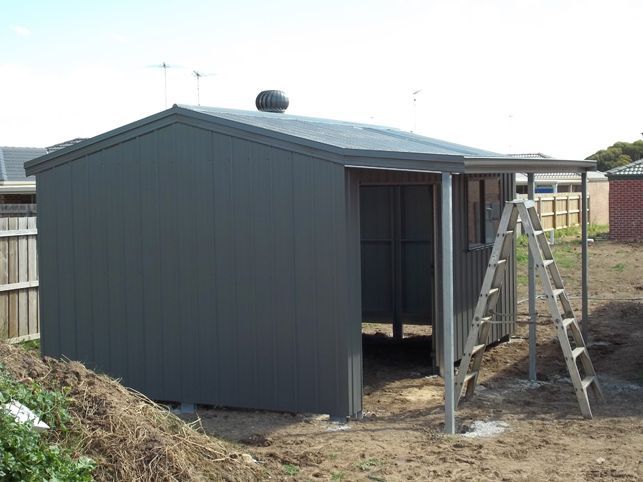 A shed with a porch and a ladder in front of it.