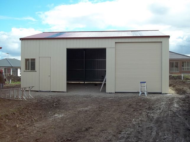 A white garage with a red roof and a ladder in front of it