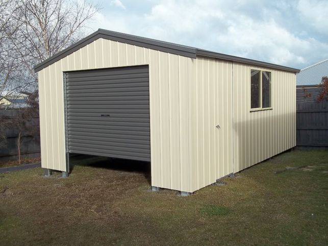 A white garage with a gray garage door is sitting in the middle of a grassy yard.