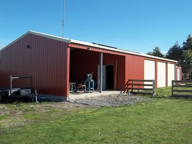 A red barn with white doors is sitting in the middle of a grassy field.
