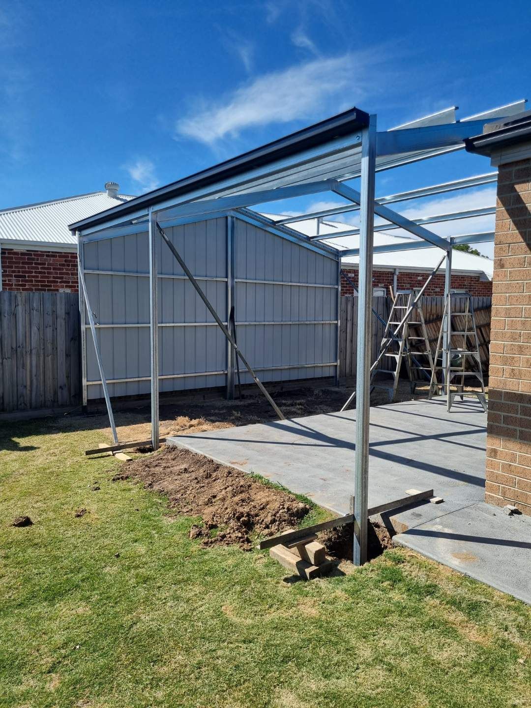 A metal structure is being built in the backyard of a house.