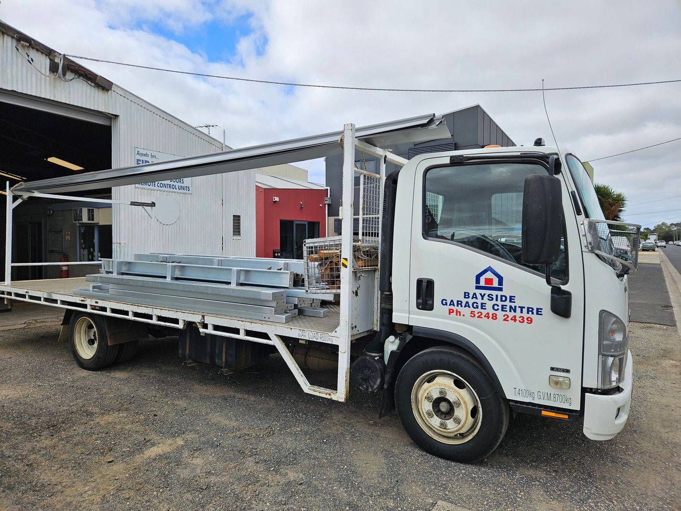 A white truck with a flat bed is parked in front of a building.