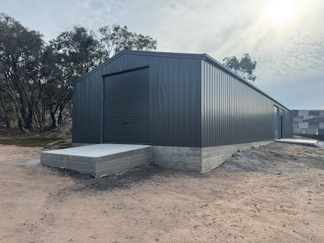 A large black metal building is sitting in the middle of a dirt field.