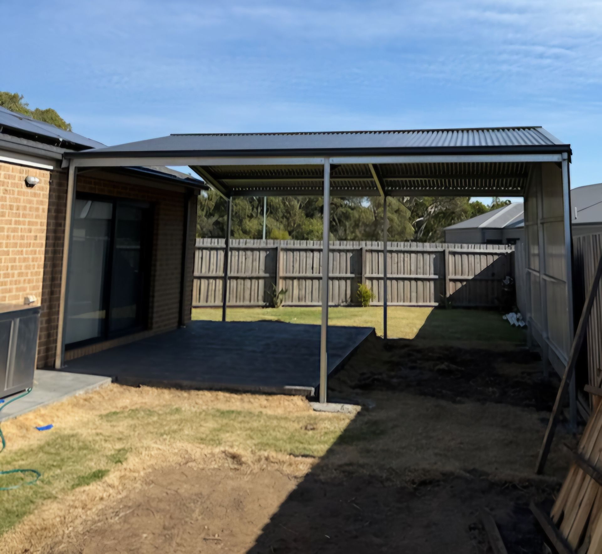 A covered area in the backyard of a house with a fence in the background.