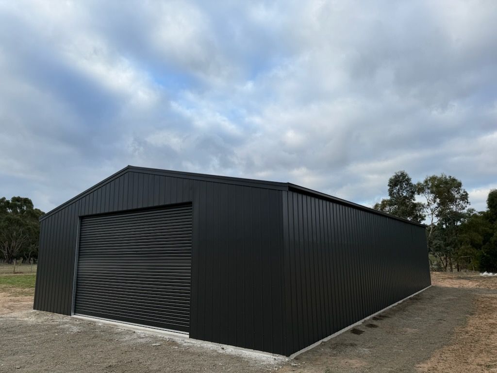 A black metal garage with a roller door is sitting in the middle of a dirt field.