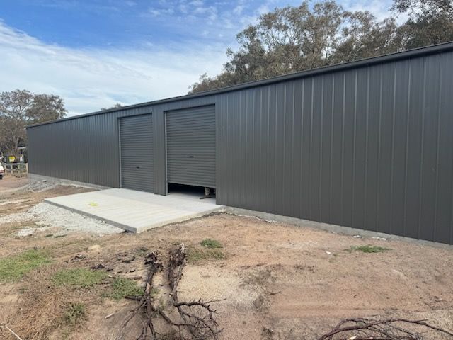 A large metal building with two garage doors is sitting in the middle of a dirt field.