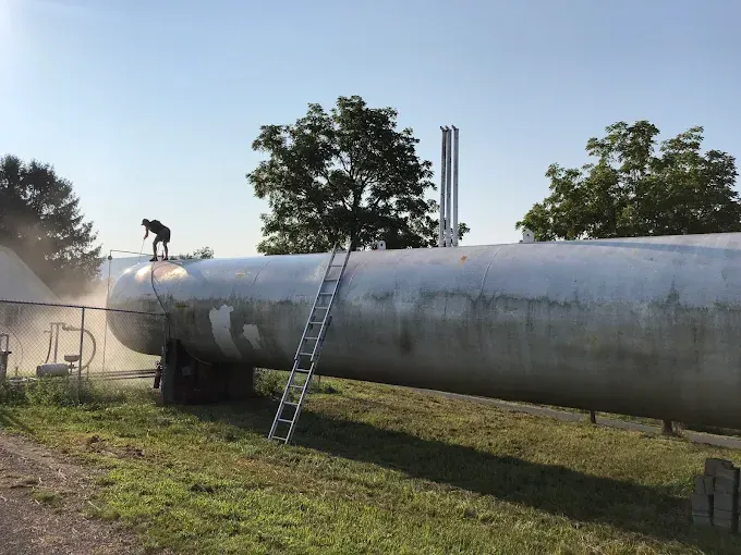 A man is standing on top of a large tank with a ladder attached to it.