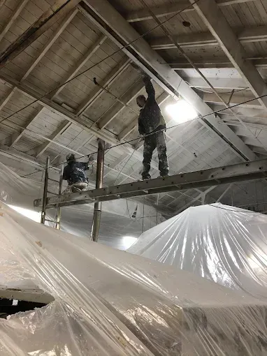 Two men are working on the ceiling of a building covered in plastic.