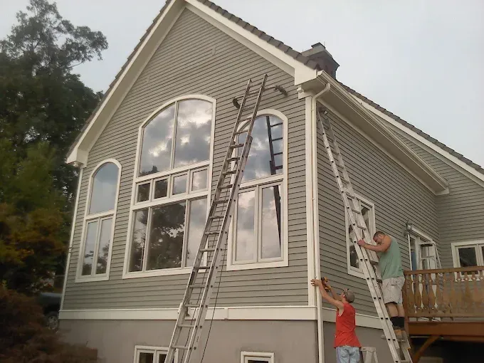 A man on a ladder paints the side of a house
