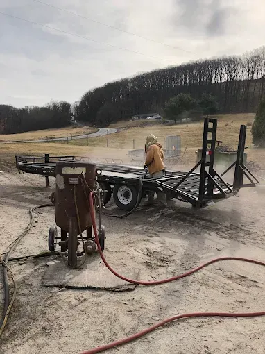 A man is sandblasting a trailer in a field.