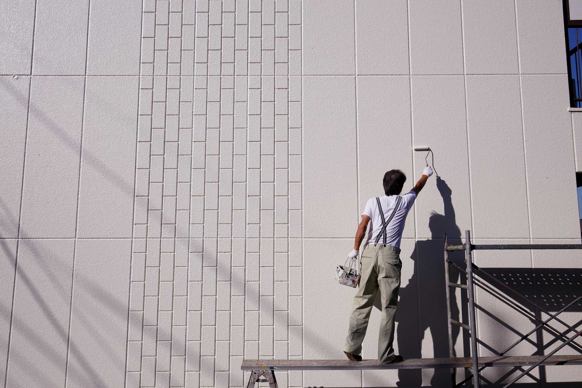 A man is standing on a scaffolding painting a wall. A man is standing on a scaffolding painting a wall.