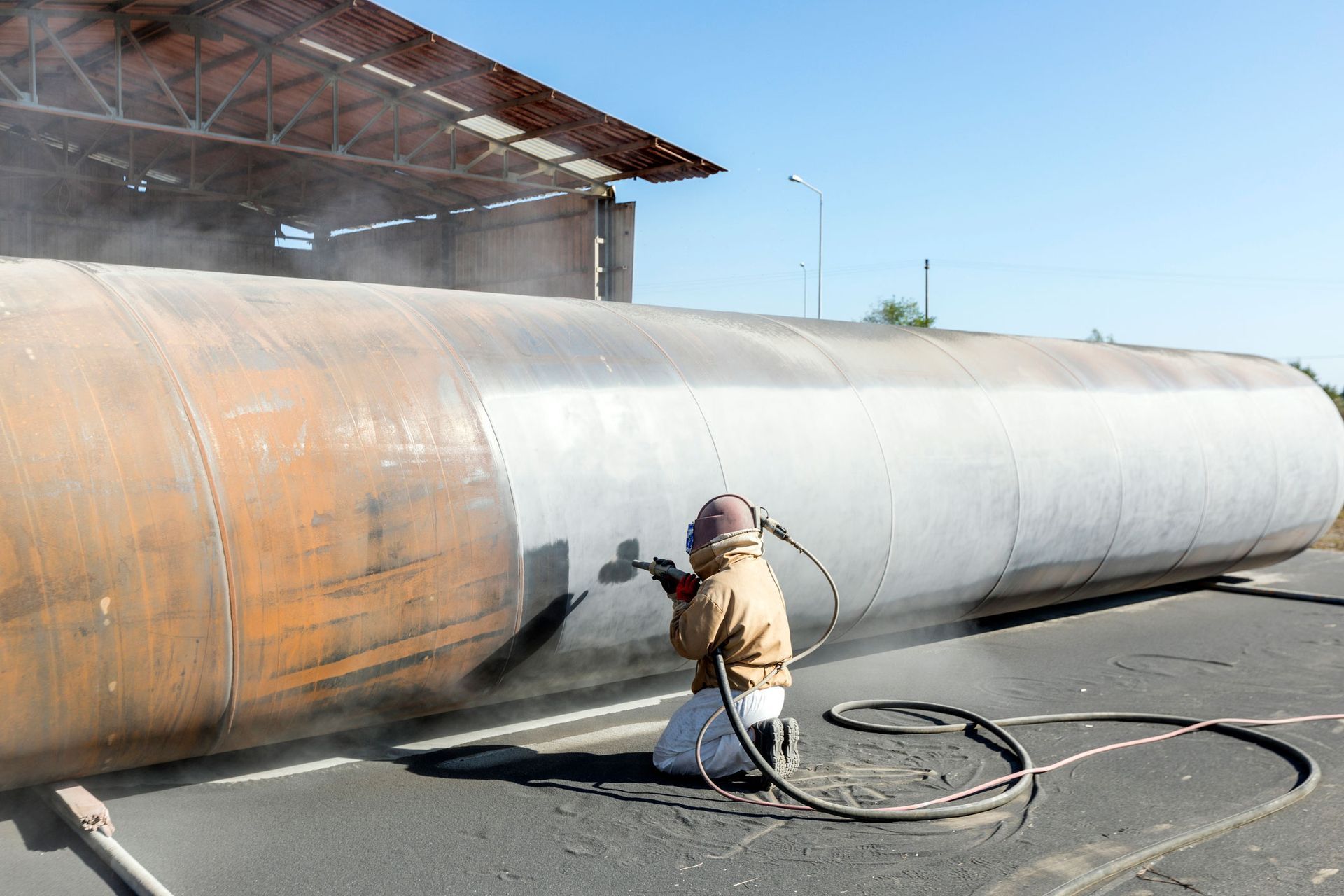 A man is sandblasting a large metal pipe. A man is sandblasting a large metal pipe.