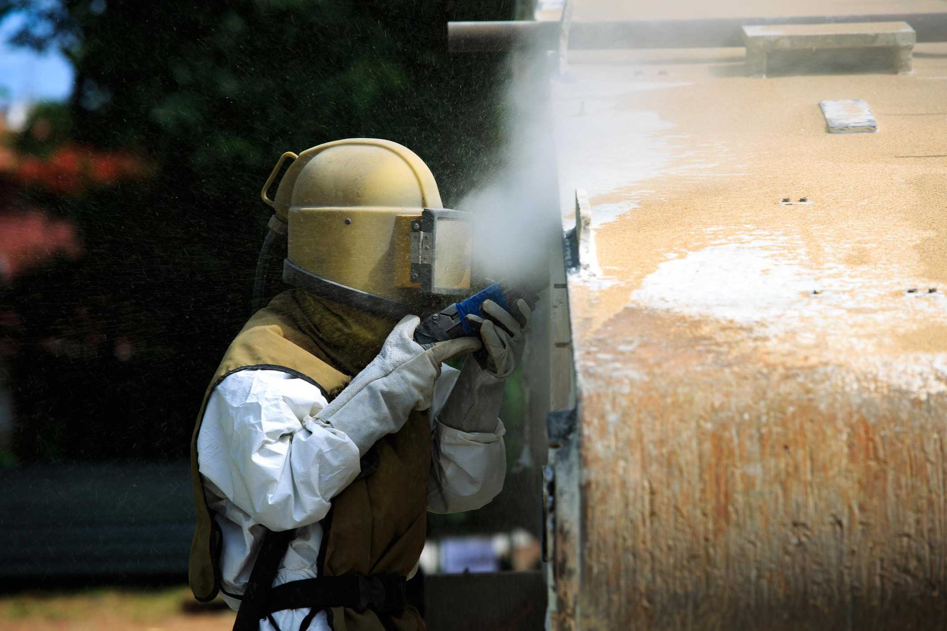 A man wearing a helmet and gloves is sandblasting a wall. A man wearing a helmet and gloves is sandblasting a wall.