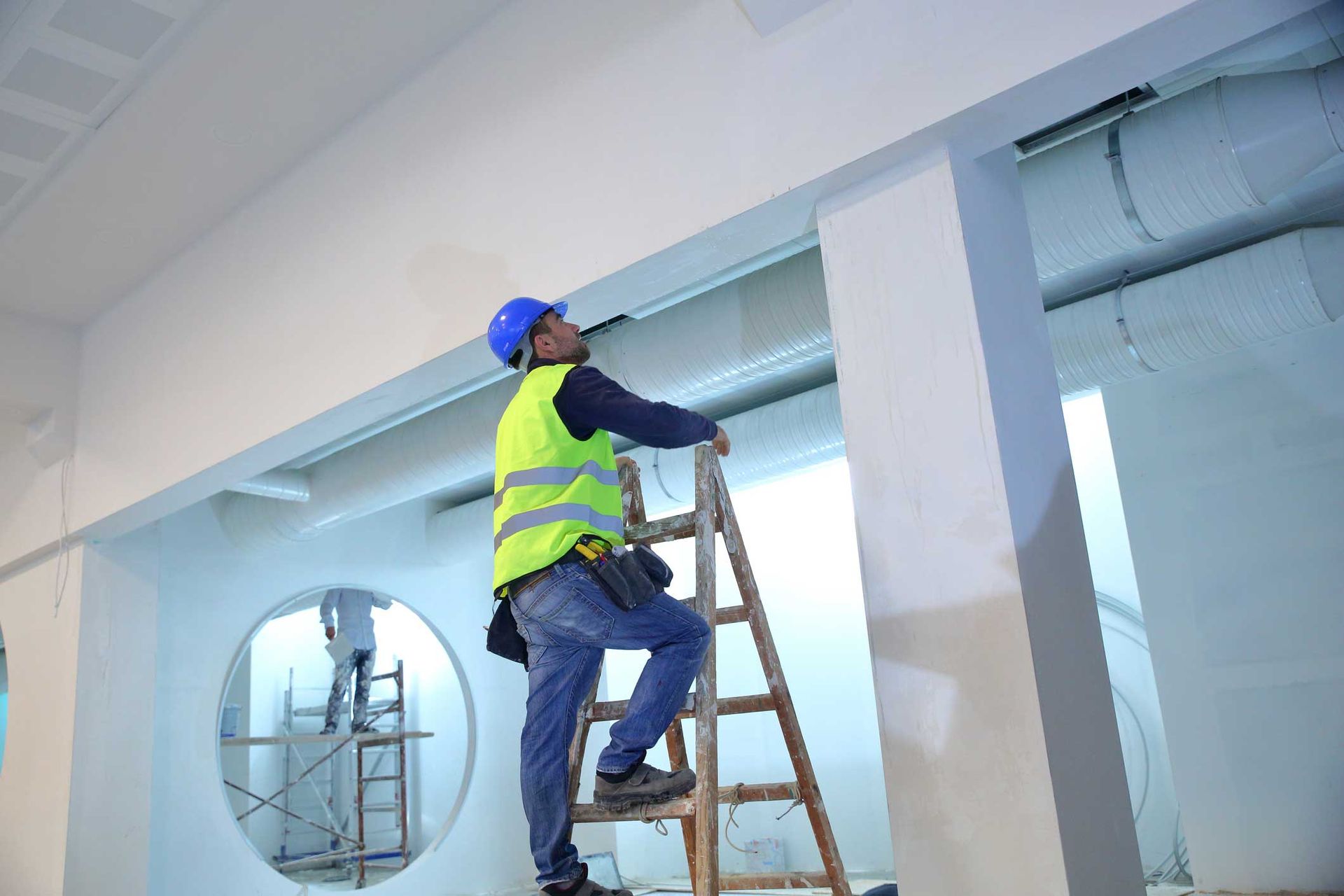 A man is standing on a wooden ladder in a room. A man is standing on a wooden ladder in a room.