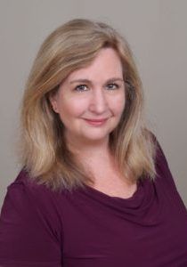 Woman with blonde hair wearing a purple shirt, smiling, headshot.