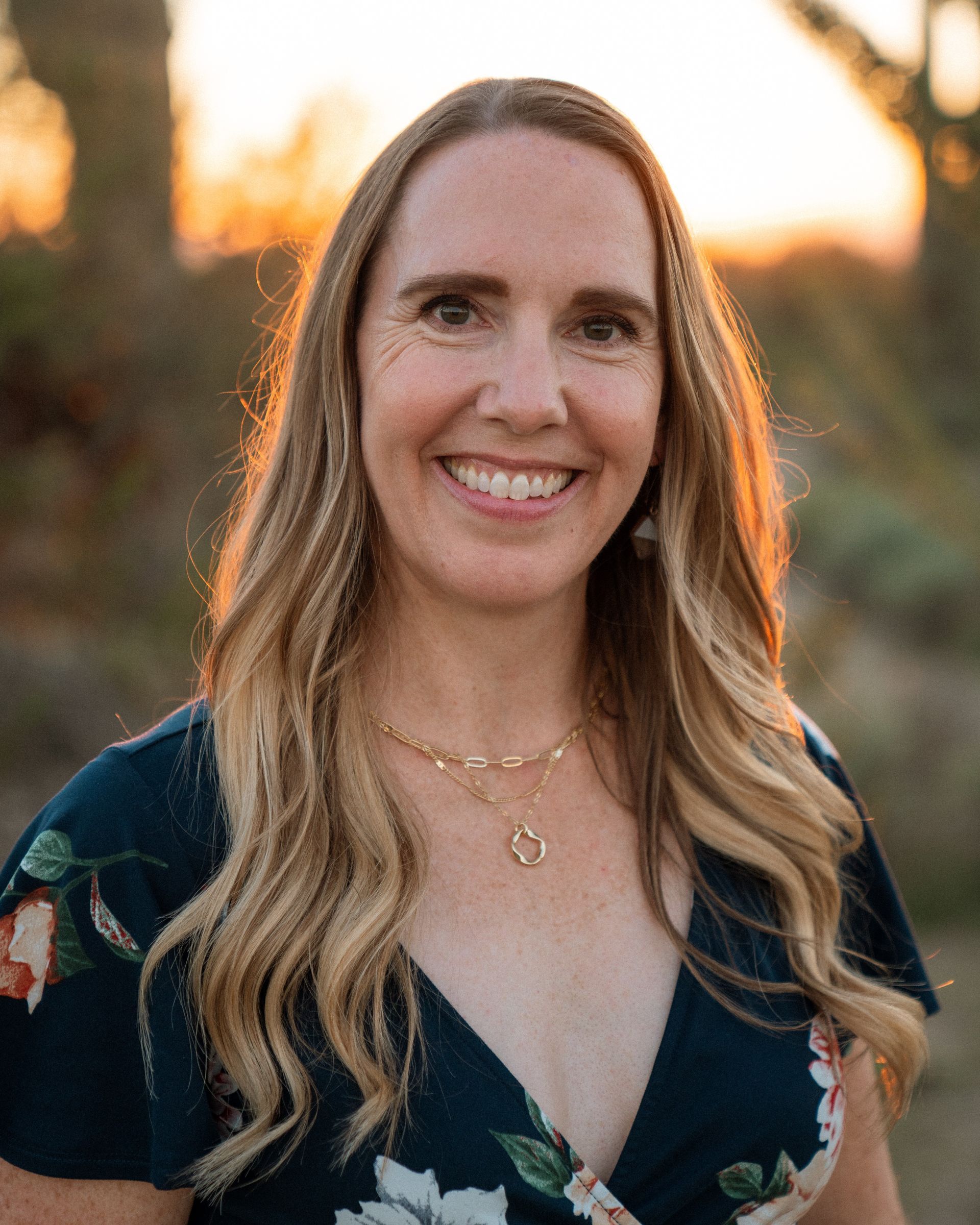 Woman with long blonde hair smiles; navy floral print top, blue and gray background.