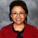 Woman with glasses smiles, wearing a red sweater and a dark blue shirt.