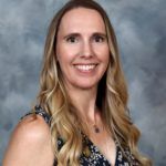Woman with long blonde hair smiles; navy floral print top, blue and gray background.