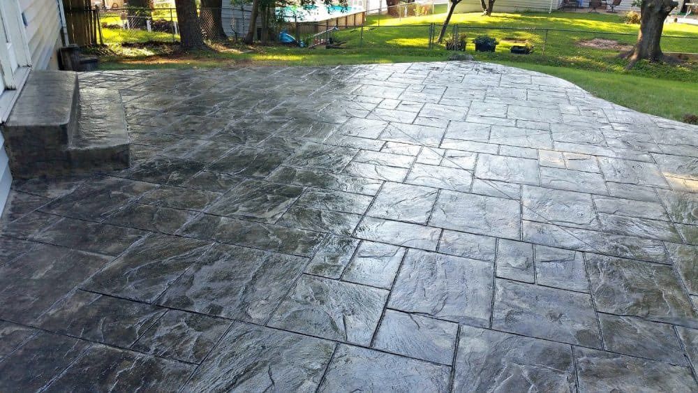 Stamped concrete patio with a dark gray, stone-like pattern, adjacent to a grassy yard.