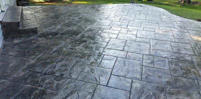 Gray concrete patio with a stone-like texture, steps on the left, and green grass in the background.