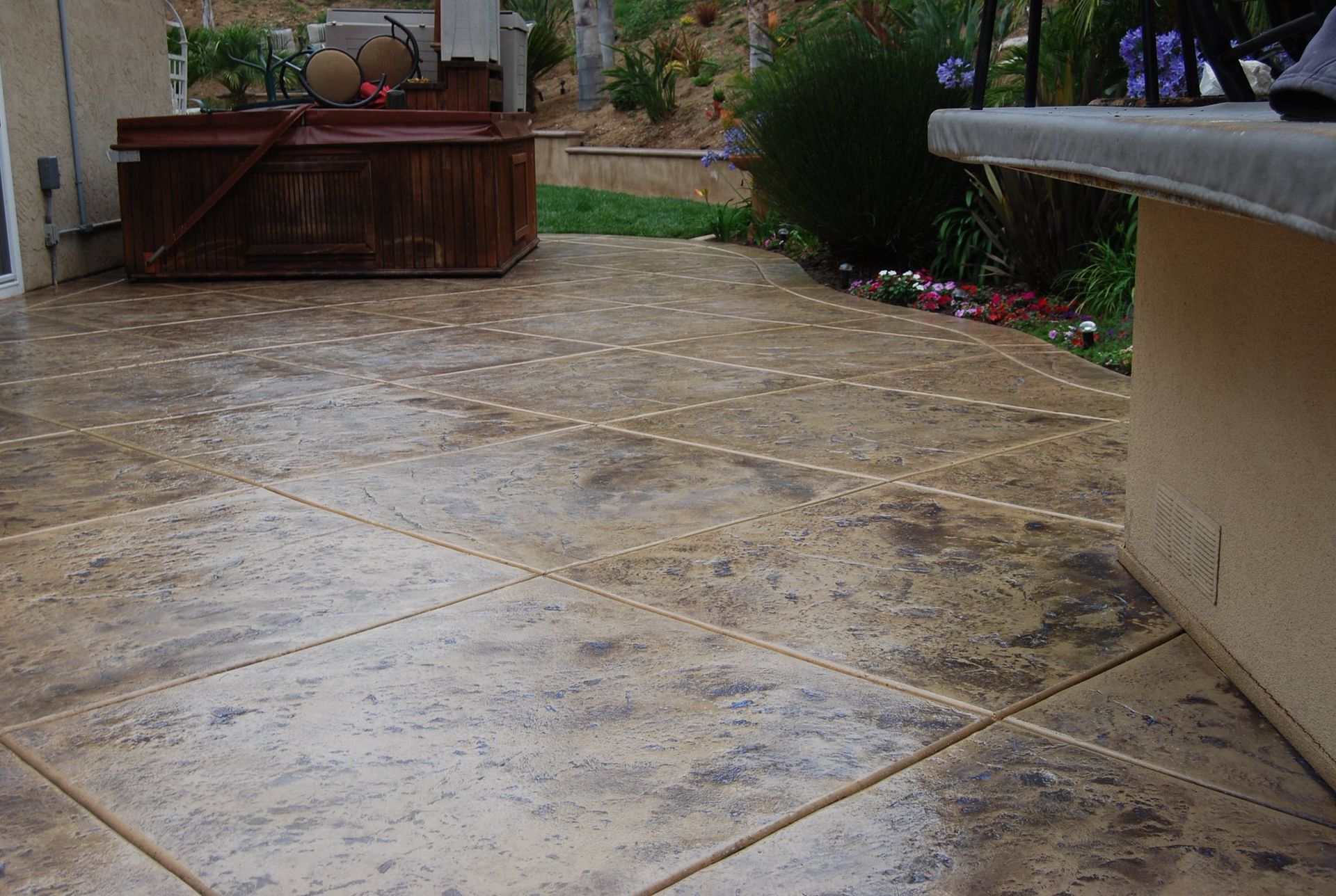 Brown stamped concrete patio with spa in the background, part of a house with a light-colored counter.