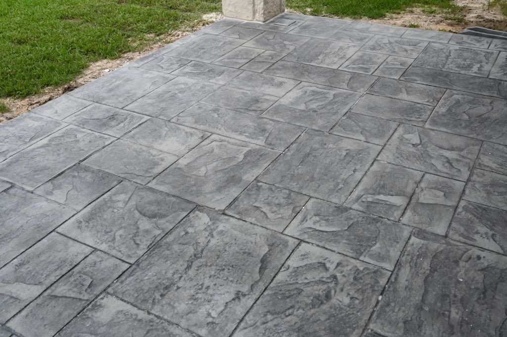Gray stamped concrete patio with rectangular stone pattern next to green grass.