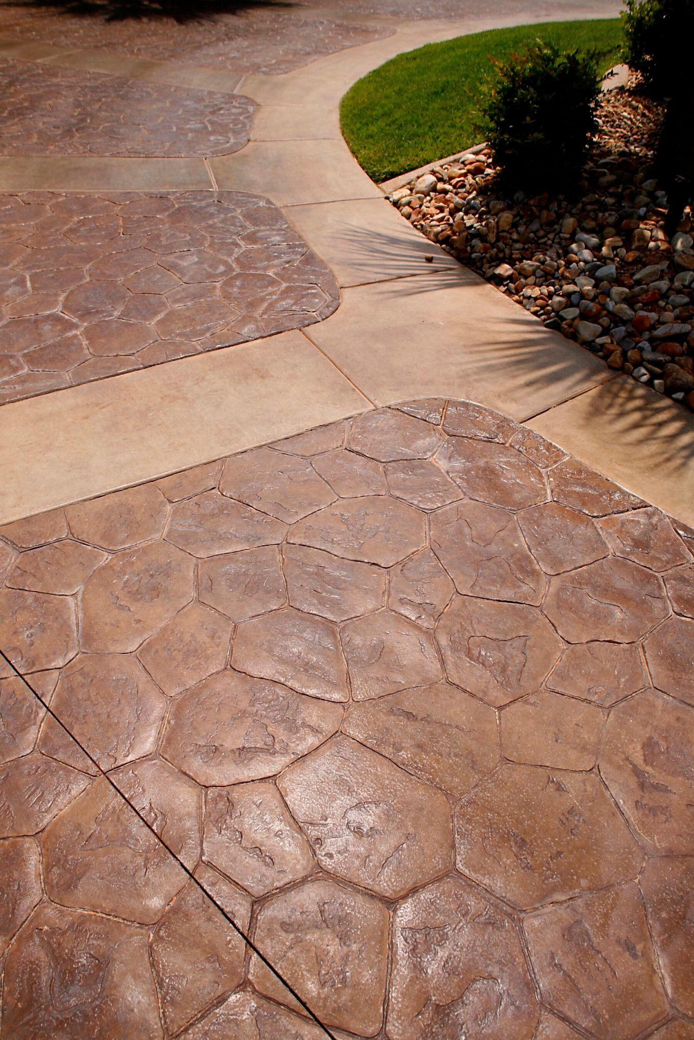 Brown stamped concrete walkway with a tan border, next to a grassy area and landscaping.