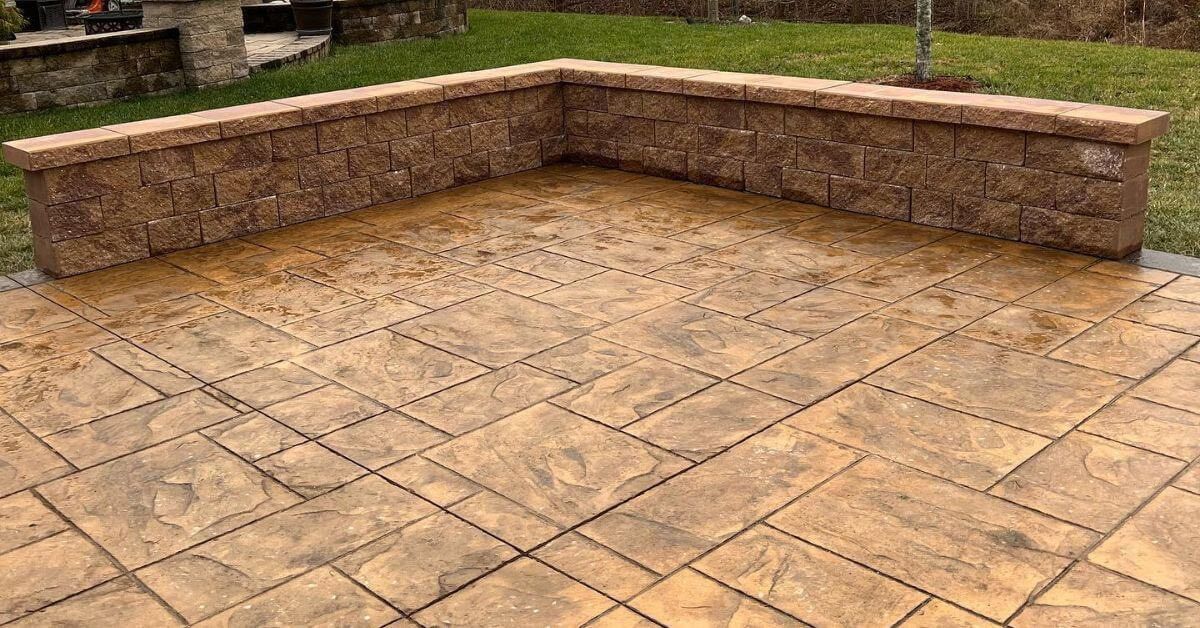 Stamped concrete patio with a low stone wall in a backyard.
