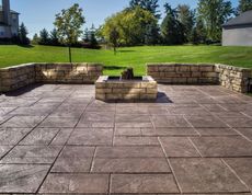 Patio with stone blocks, fire pit, and a grass yard in daylight.