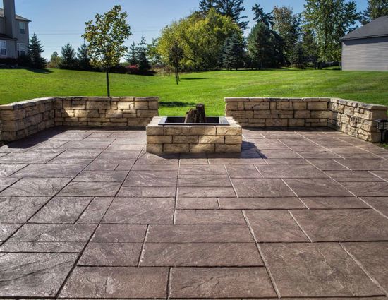 A stamped concrete patio with a fire pit and stone retaining walls in a backyard setting.