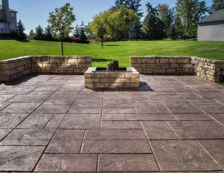 A stamped concrete patio with a fire pit and stone retaining walls in a backyard setting.
