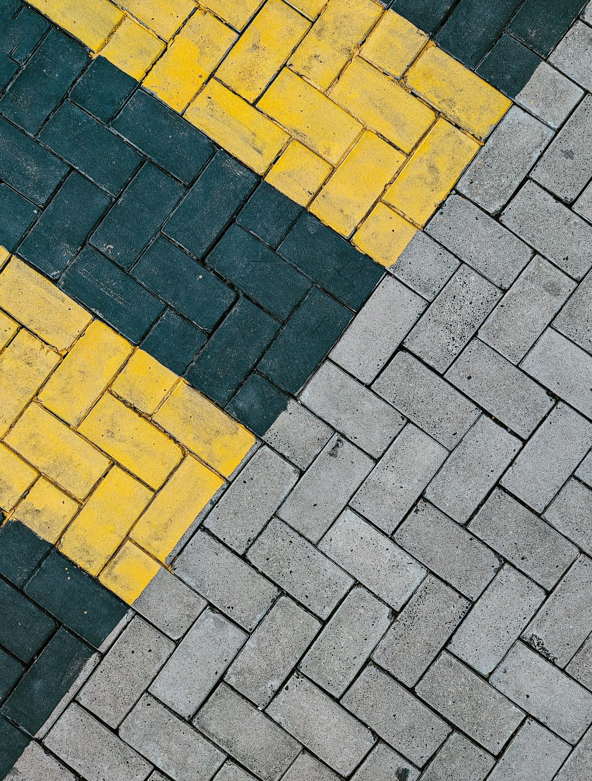 Brick pavement with yellow and dark green diagonal stripes, and grey bricks.