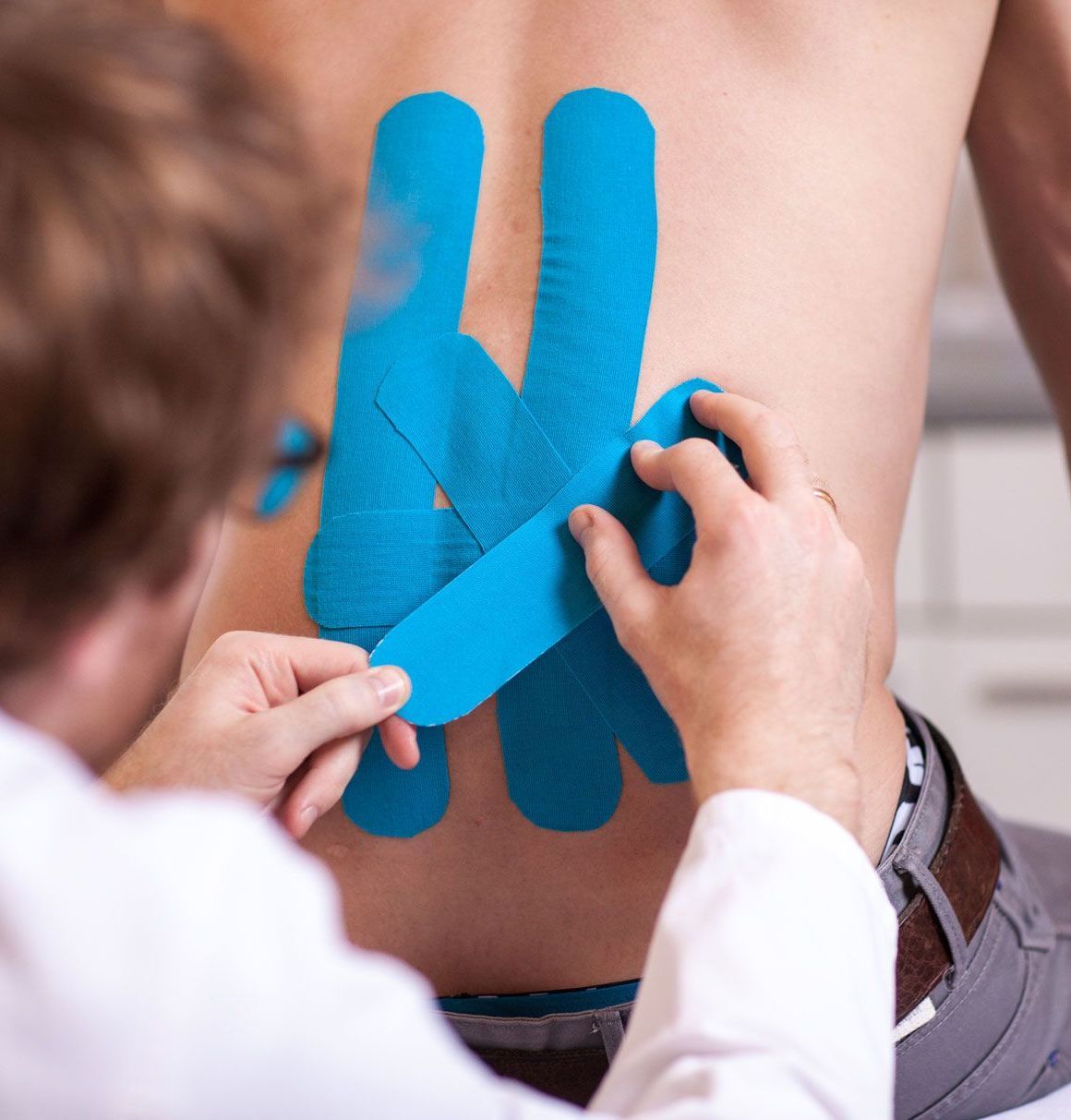 Elastische Tapes werden von Dr. Kramer auf dem Rücken eines Patienten angebracht