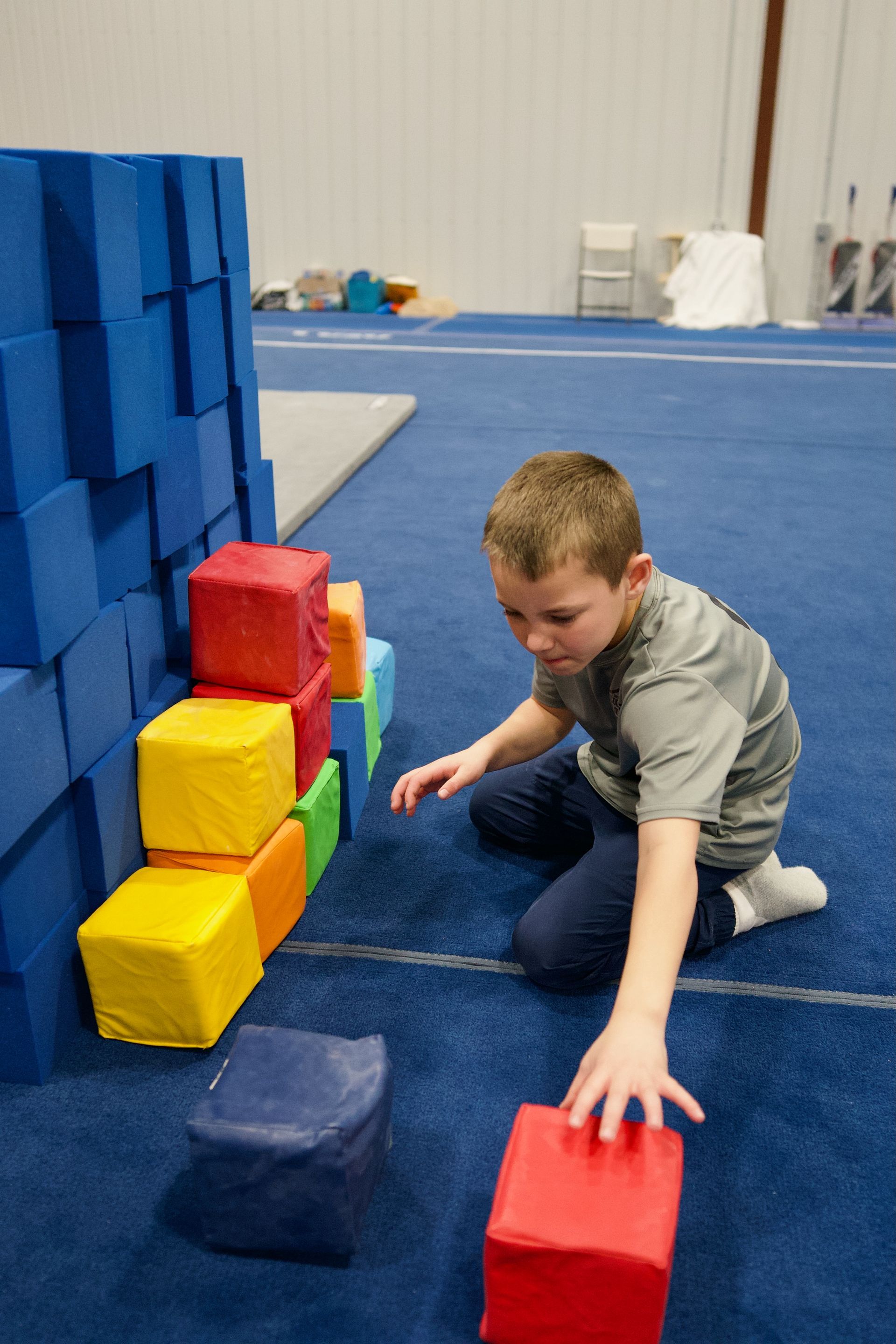 Child exercising on a seated machine in a gym, with black equipment and purple mats nearby.