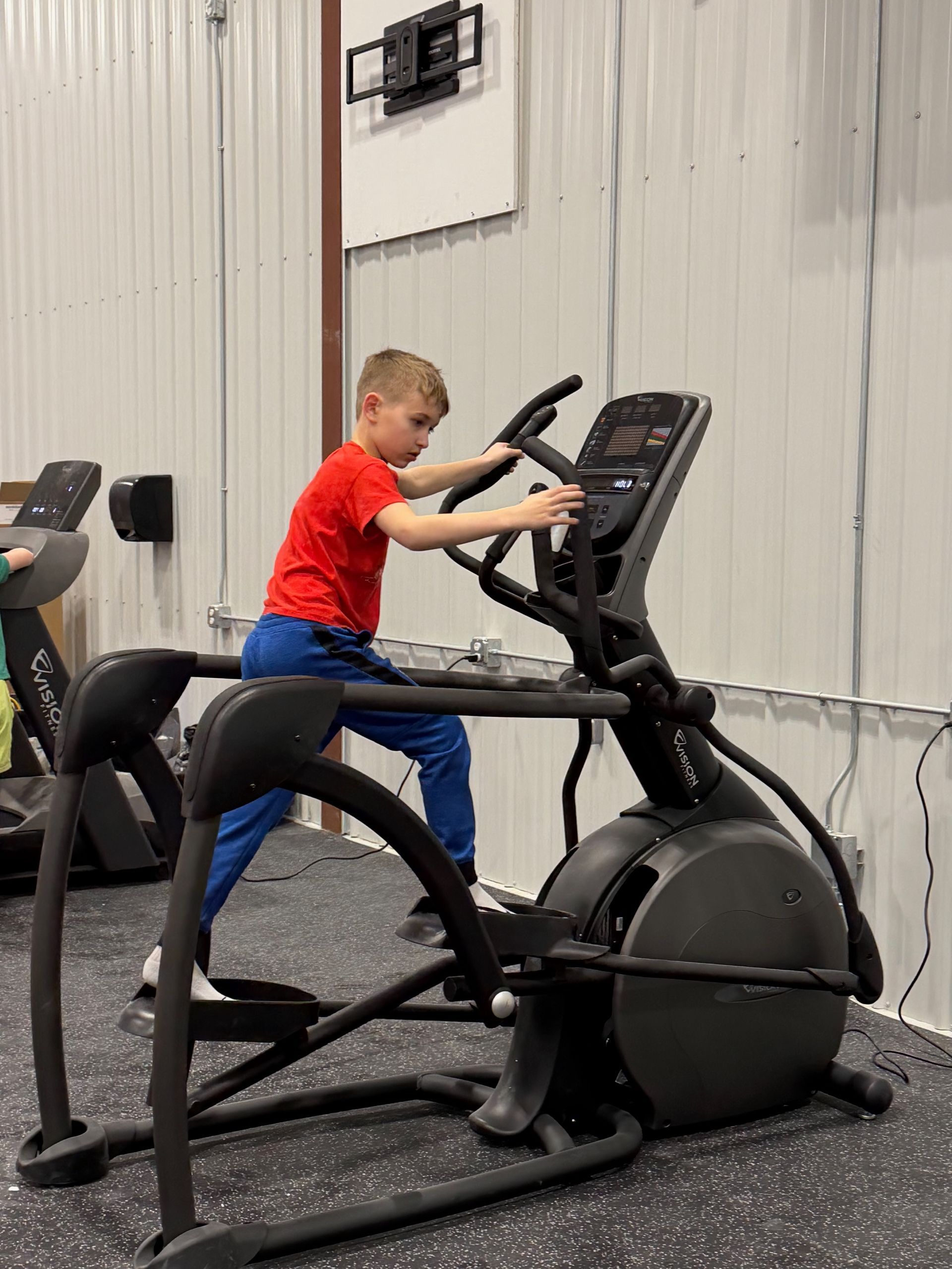 Child in red shirt using an elliptical machine in a gym
