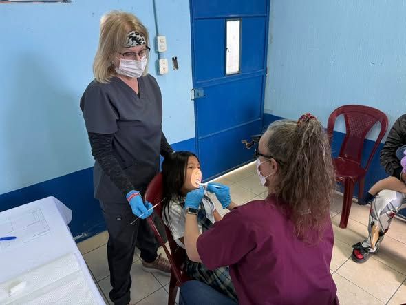 Two medical professionals in scrubs examine a patient's throat in a clinic setting.