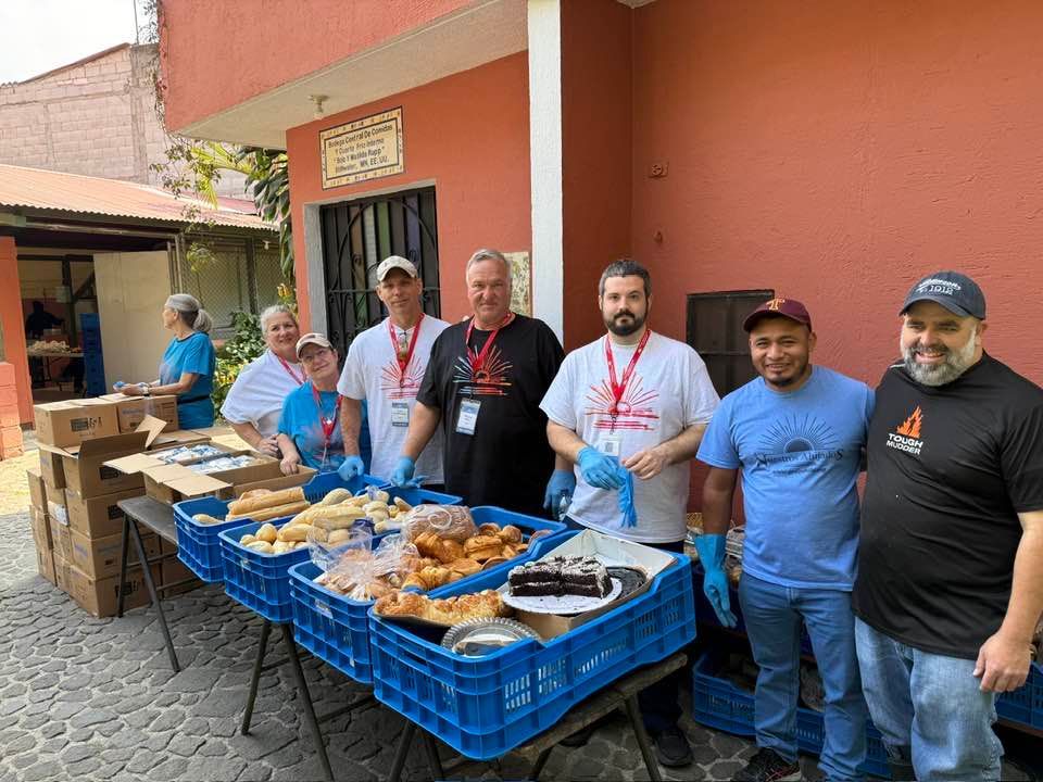 Volunteers in matching shirts getting ready to distribute bread and pastries at an outdoor event near a red building.